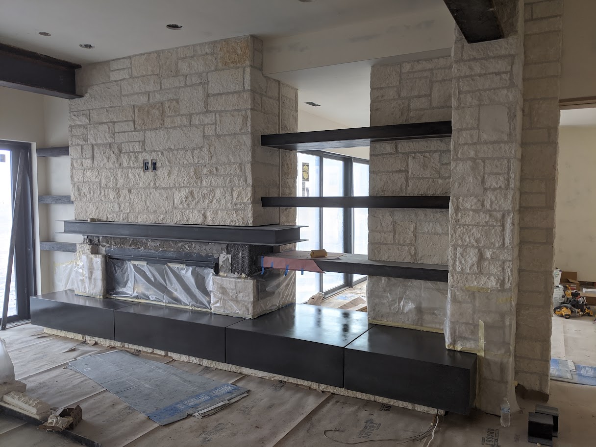 Cast limestone fireplace wall with steel shelves during construction