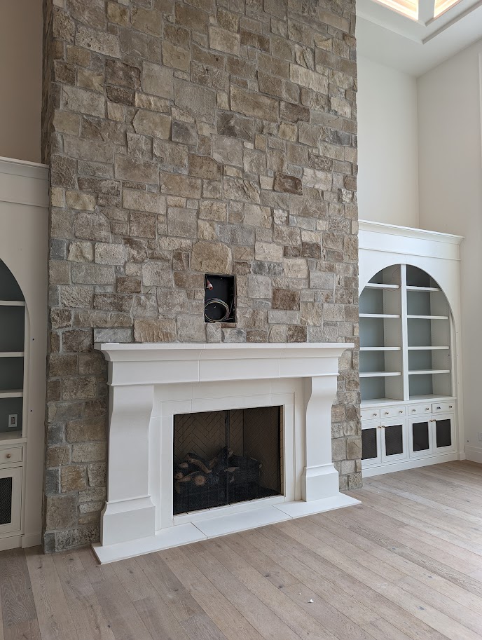 Traditional white cast limestone fireplace mantel against a stone chimney wall
