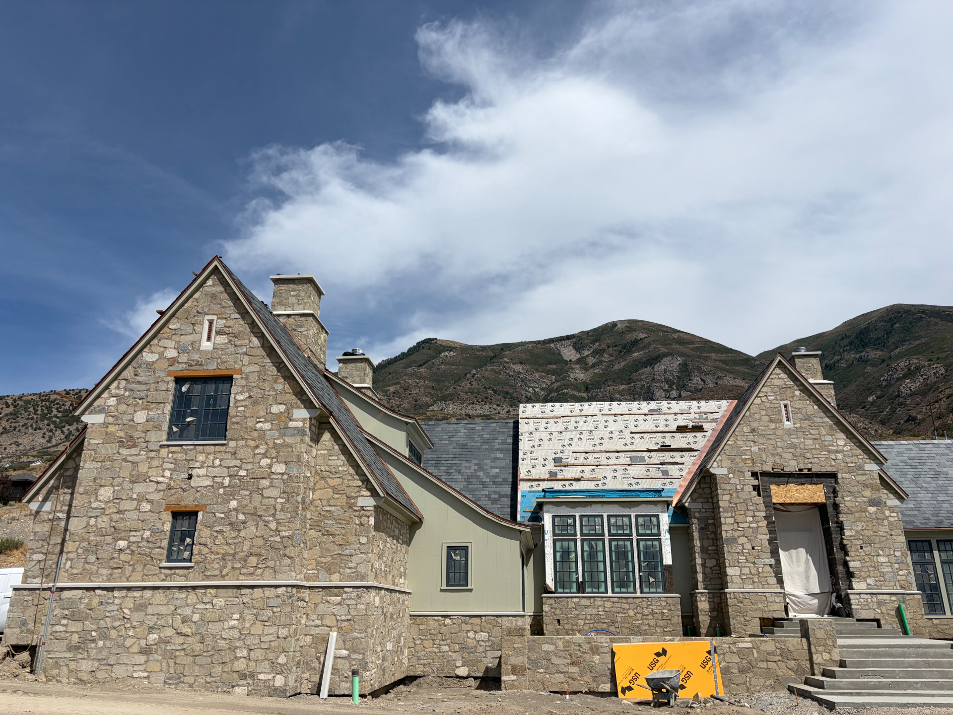 Stone masonry estate under construction with stucco gables and mountain views