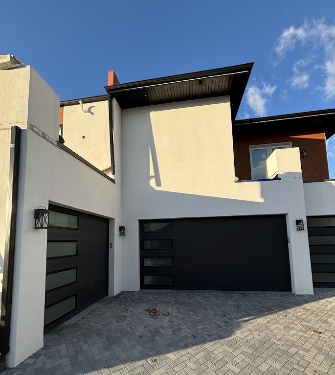 Modern white stucco garage elevation with black doors and clean parapet lines