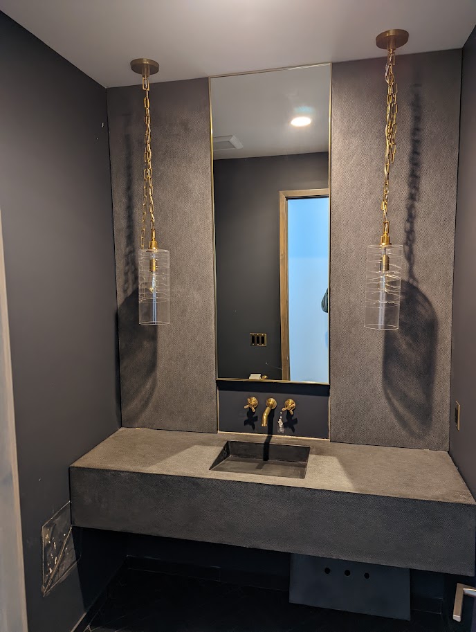 Cast stone floating vanity in a dark powder room with brass fixtures